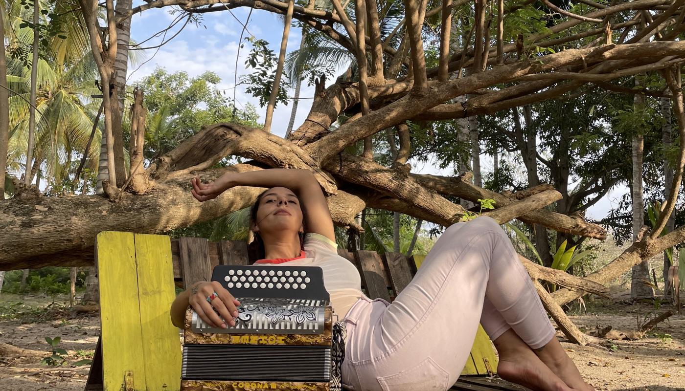 A woman lounging on a bench in front of a large tree with an accordion